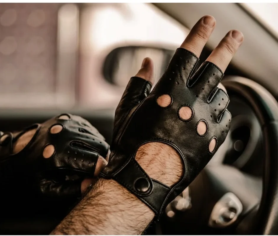 Person wearing black fingerless leather driving gloves with knuckle holes and snap button closure while holding a steering wheel.